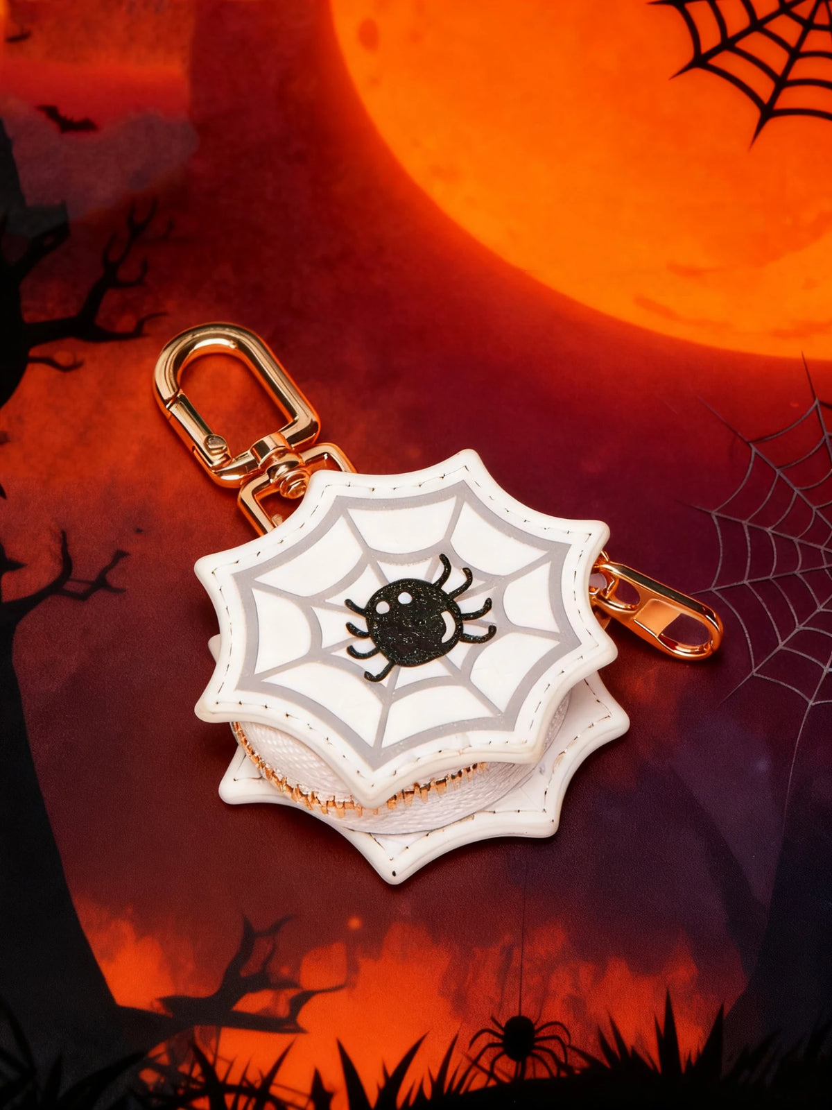 Llavero monedero de calabaza tono dorado con diseño de araña negra sobre fondo naranja y oscuro.