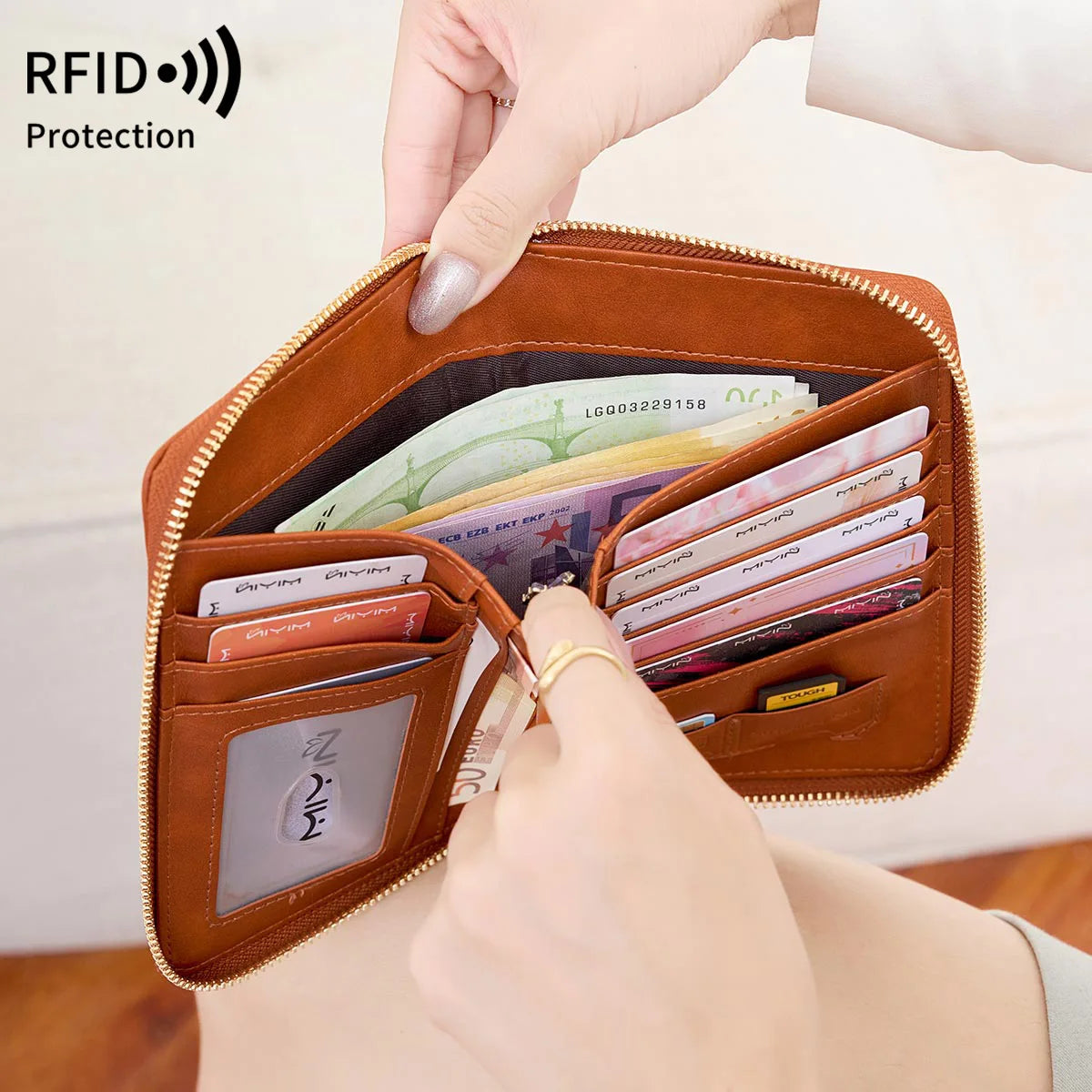 A hand is opening a brown leather RFID blocking travel wallet to show protected credit cards and identification documents.