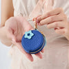 A hand holds a blue quilted coin purse keychain with a light blue star charm against a pink garment.