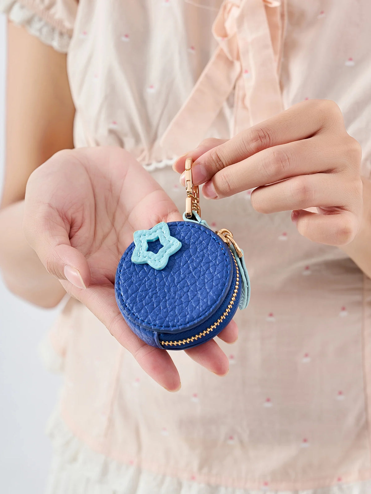 A hand holds a blue quilted coin purse keychain with a light blue star charm against a pink garment.