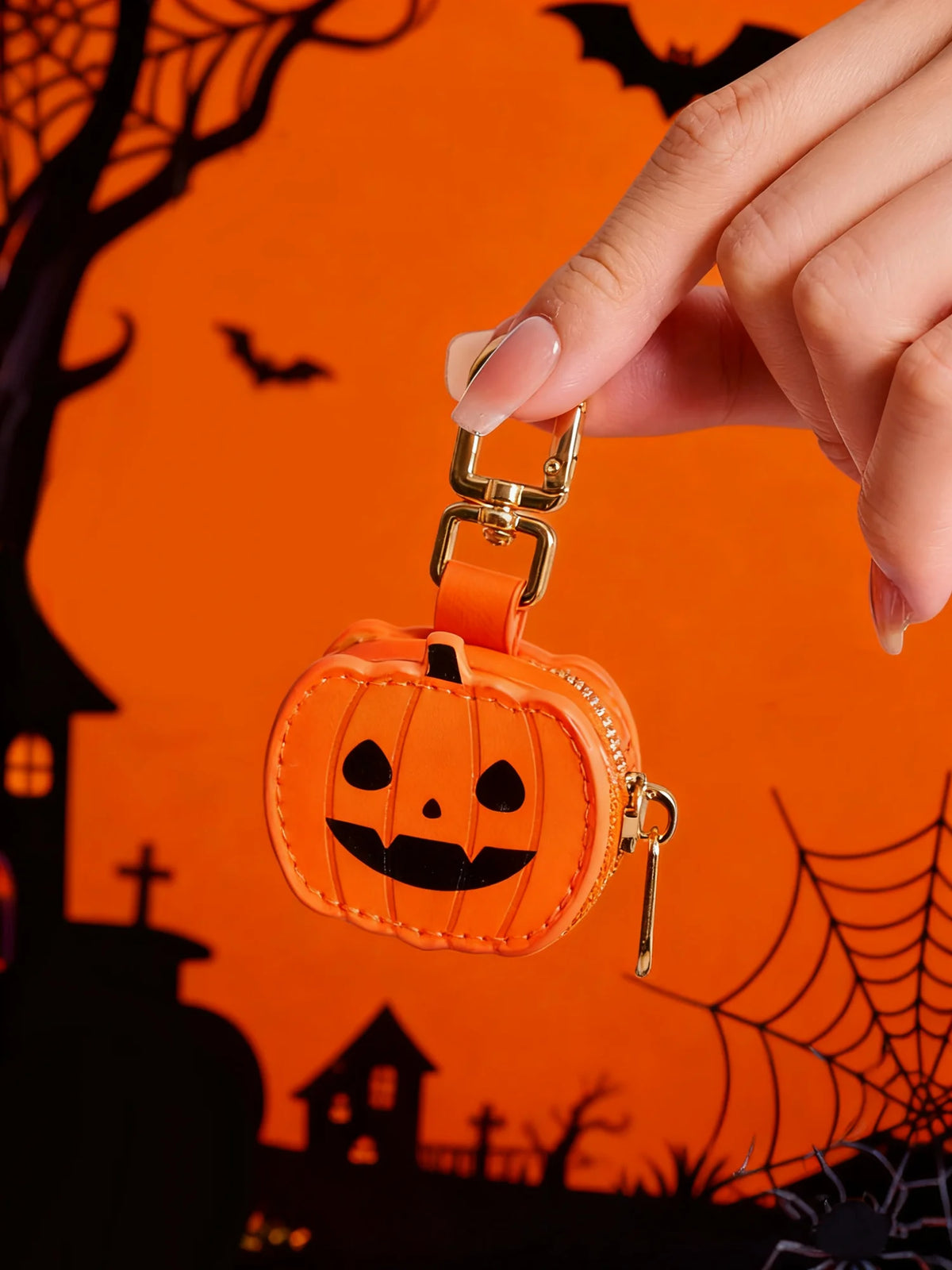 Llavero de calabaza naranja tallada con cara sonriente negra, sostenido por una mano contra fondo naranja.