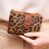 A brown leopard print women's wallet with a leather flap and gold-toned zipper is held in a hand.