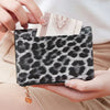A hand holds a black leopard print women's wallet with a gold zipper and a folded banknote.