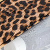 A close-up of a leopard print fabric being placed inside a clear cosmetic bag.