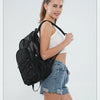 A young woman wearing a black mesh backpack and denim shorts poses against a light gray background.