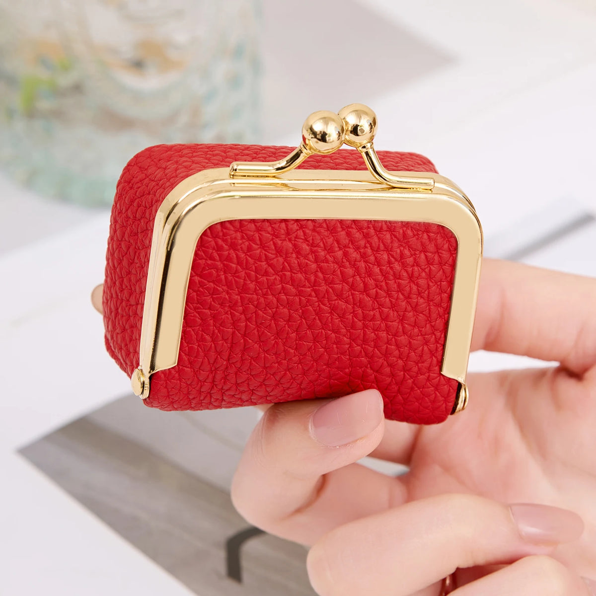 Una caja de almacenamiento de joyas de terciopelo rojo mini con detalles dorados sostenida en la mano de una persona.