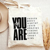 A white canvas tote bag with black text that reads YOU ARE ENOUGH BRAVE WORTHY LOVED AMAZING STRONG CAPABLE SMART KIND