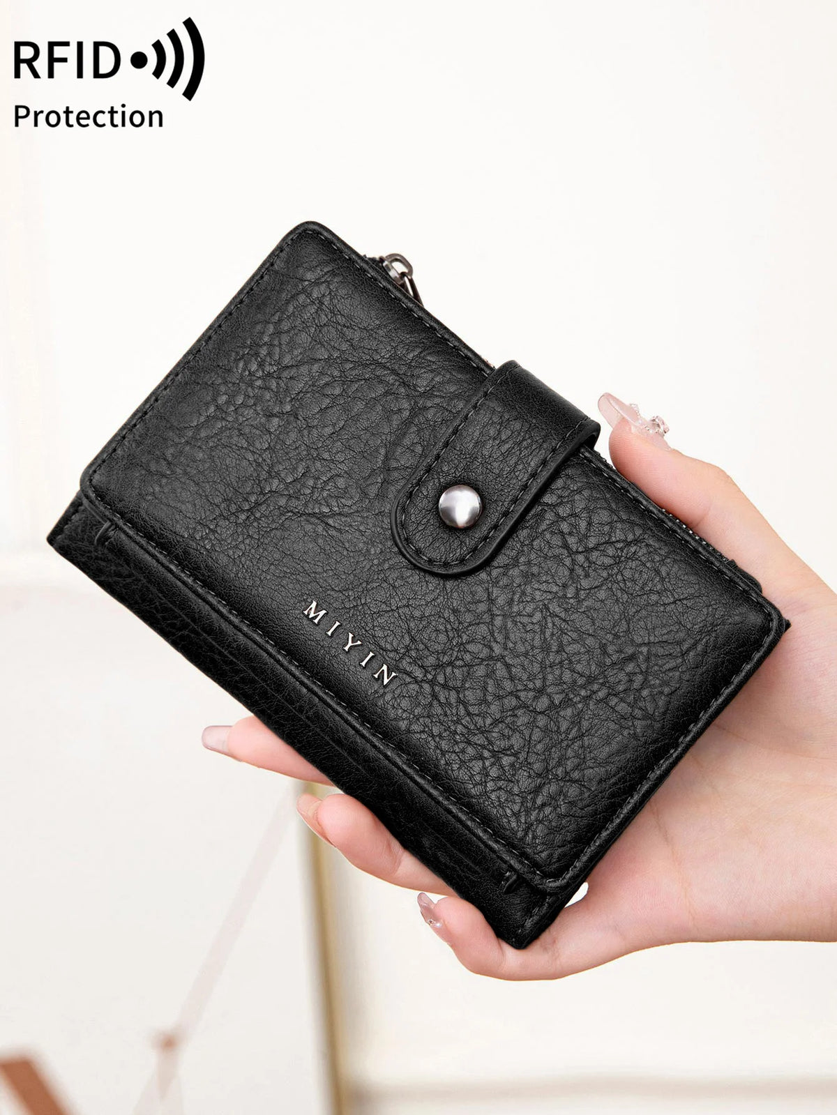 A hand holds a black leather clutch wallet with an RFID protection feature.