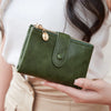 A hand holds a dark olive green minimalist women's foldable wallet with a gold zipper.