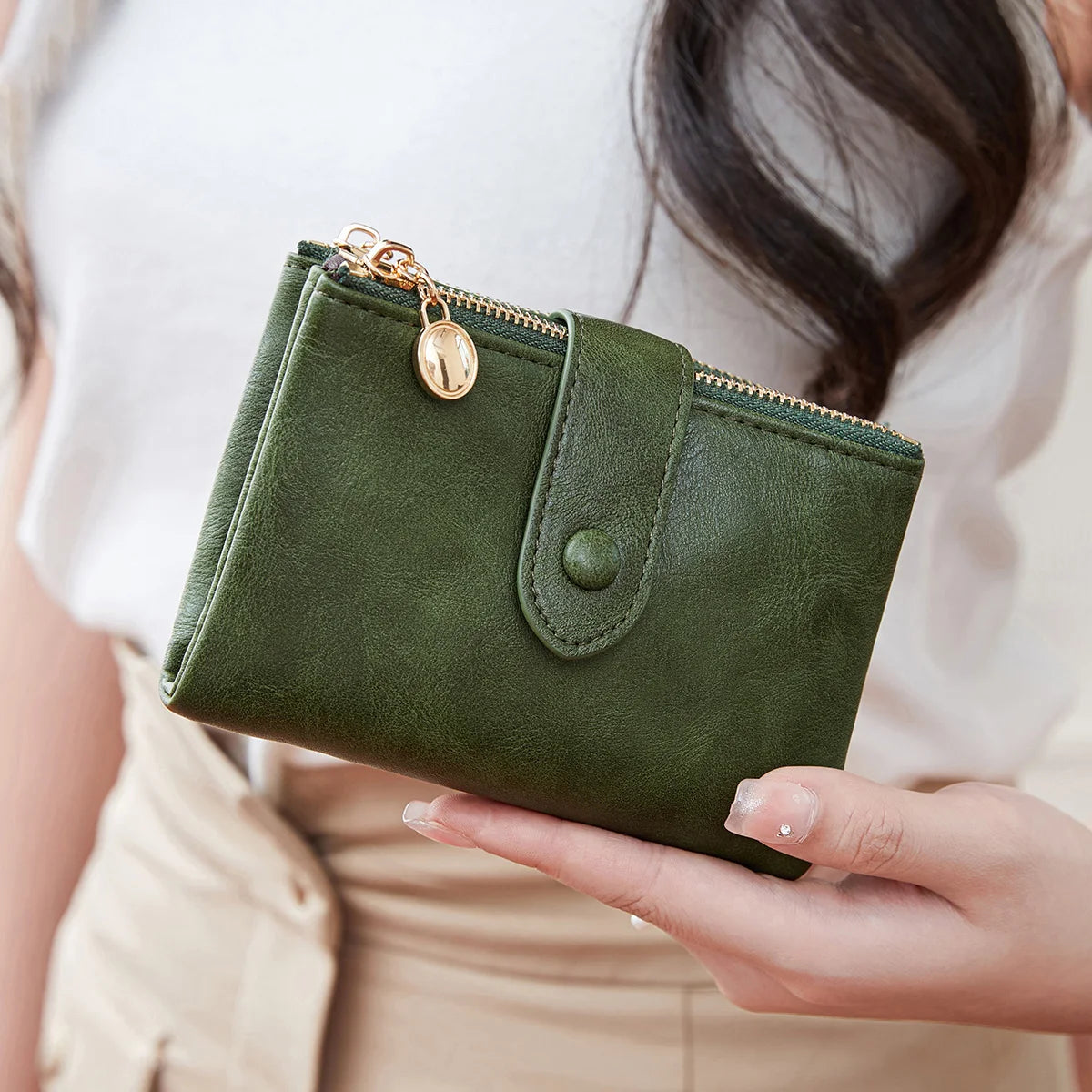 A hand holds a dark olive green minimalist women's foldable wallet with a gold zipper.