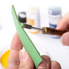 Une main tient un outil de peinture à bord vert en cuir avec un pinceau, à côté de flacons cosmétiques.