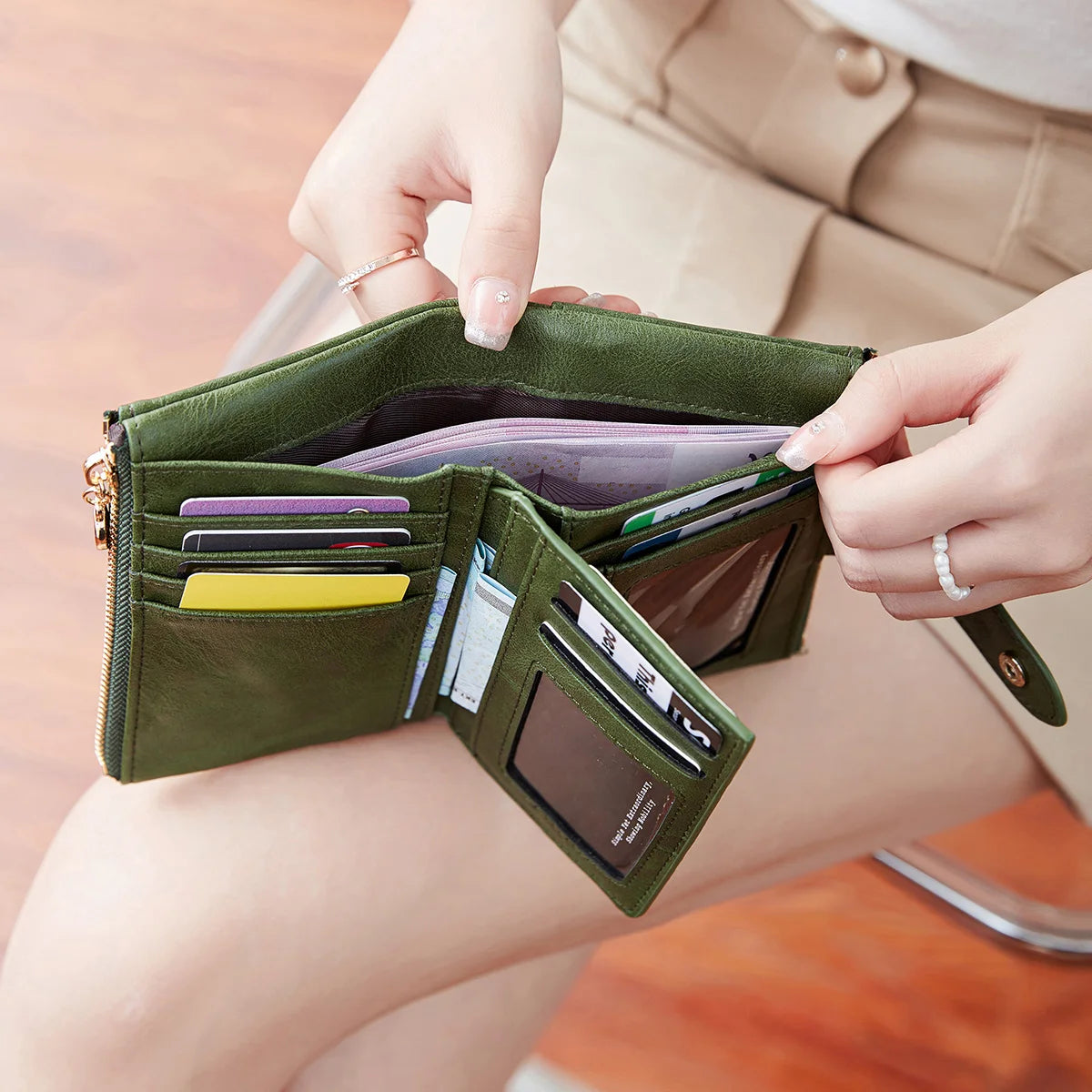 A hand opens a dark olive green minimalist women's foldable wallet showing various cards and cash inside.