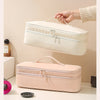 A hand is lifting a cream-colored storage bag for a hair dryer, with a pink version resting on a white surface.