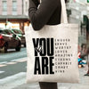 A white canvas tote bag with black text that reads YOU ARE ENOUGH BRAVE WORTHY LOVED AMAZING STRONG CAPABLE SMART KIND