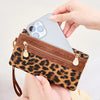 A hand holds a brown leopard print clutch wallet with a zipper and a wristlet strap, displaying a smartphone.