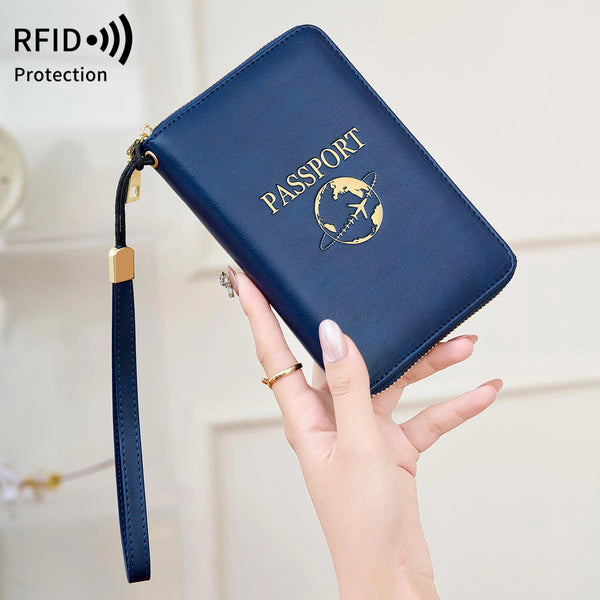 A hand holds a dark blue RFID blocking passport wallet with a gold emblem and a strap.