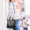 A woman is holding a black crocodile-embossed leather tassel shoulder bag in a casual outdoor setting.