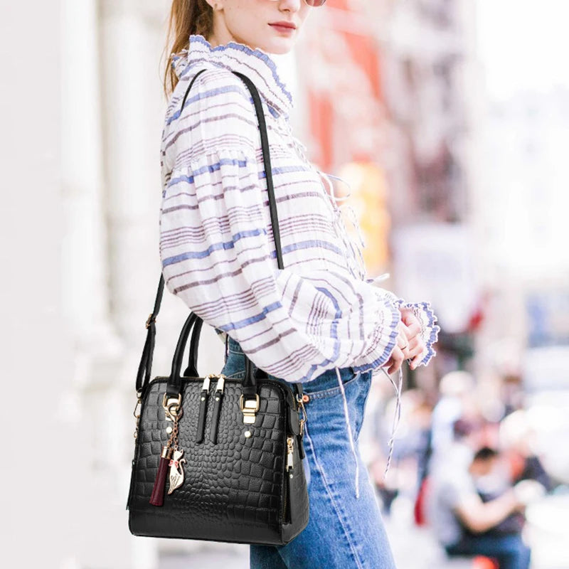 A woman is holding a black crocodile-embossed leather tassel shoulder bag in a casual outdoor setting.
