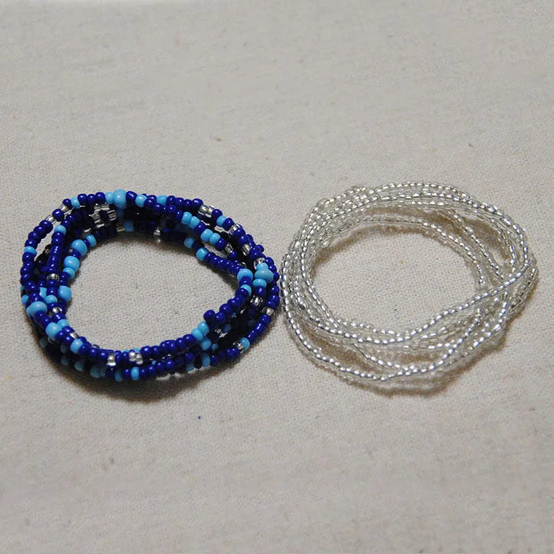 Two strands of colorful belly bead chains, one dark blue and the other clear, laid out on a light surface.