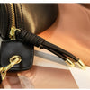 A black PU leather crossbody sling bag with gold hardware resting on a tan fabric background.