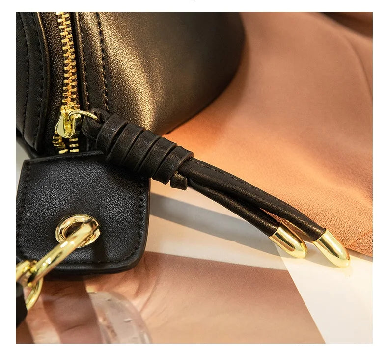 A black PU leather crossbody sling bag with gold hardware resting on a tan fabric background.