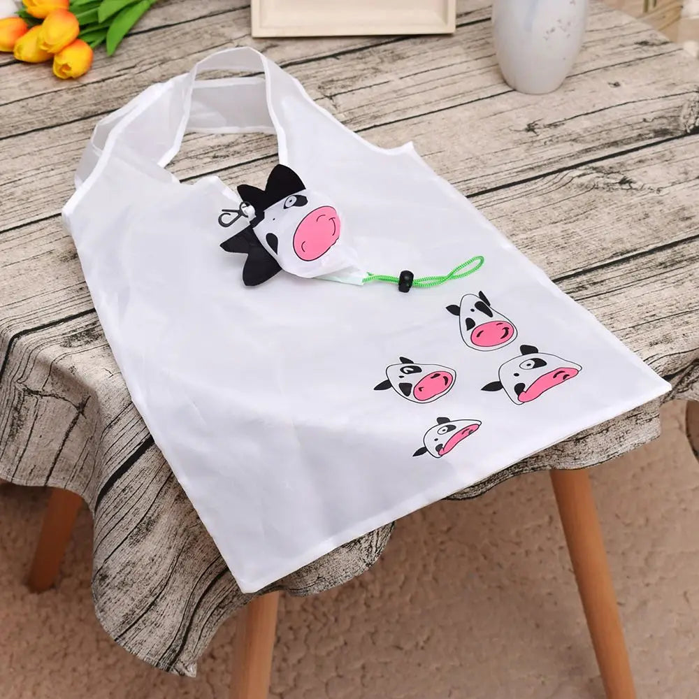 Sac de shopping cartonné blanc et pliable, écologique, avec un motif de vache noire et rose, posé sur une table en bois.