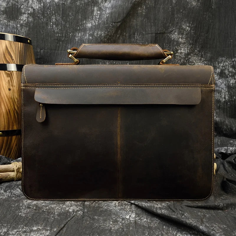A dark brown vintage Crazy Horse leather briefcase with a top handle and laptop compartment resting on a dark fabric.