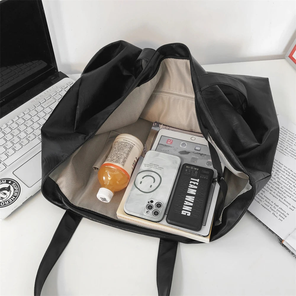 A black oversized PU leather tote bag is open, revealing a laptop and several electronic devices inside.