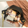 A black PU leather crossbody sling bag filled with perfume bottles and a white cosmetic item, resting on a beige fabric.