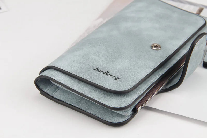 A light blue suede card holder wallet with a black trim and silver clasp resting on a white surface.