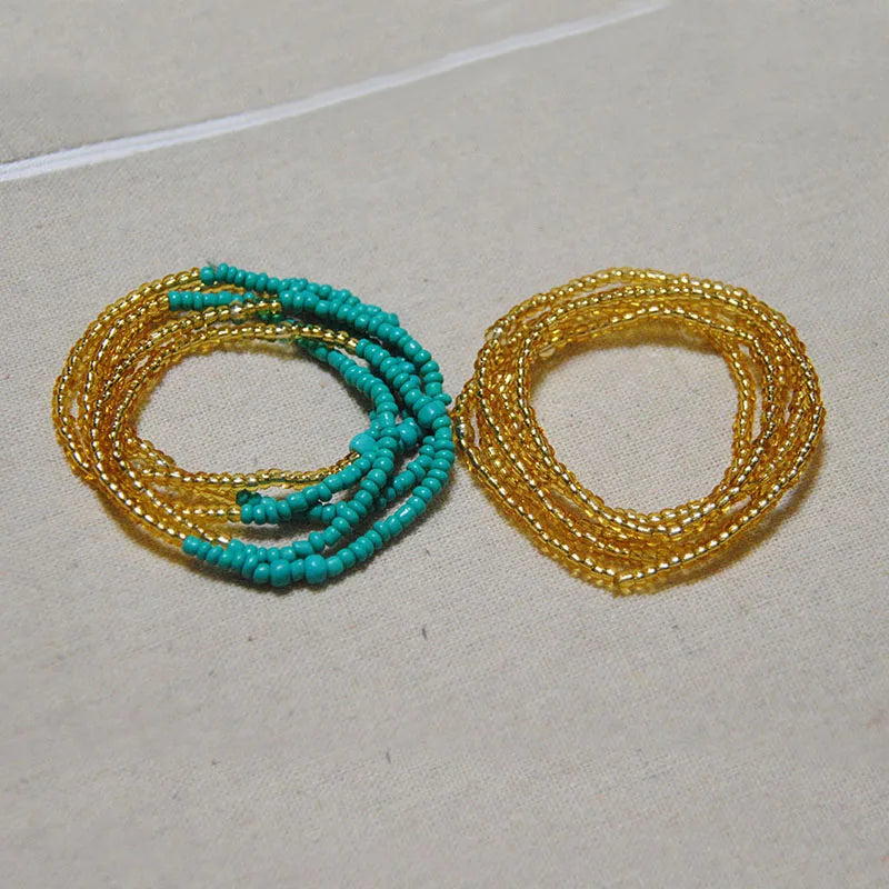 Two strands of colorful belly bead chains, featuring turquoise and gold beads, laid out on a light surface.