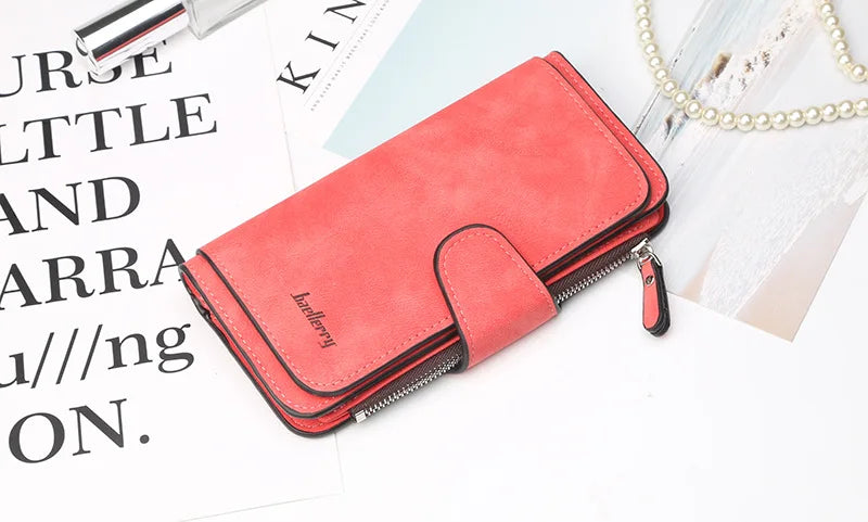 A coral red card holder wallet with a zipper is shown next to some papers and a pearl necklace.