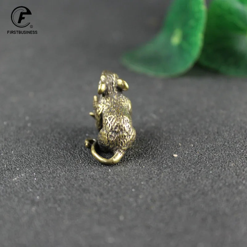 A vintage brass rat figurine used for good luck and home decor, resting on a dark surface.