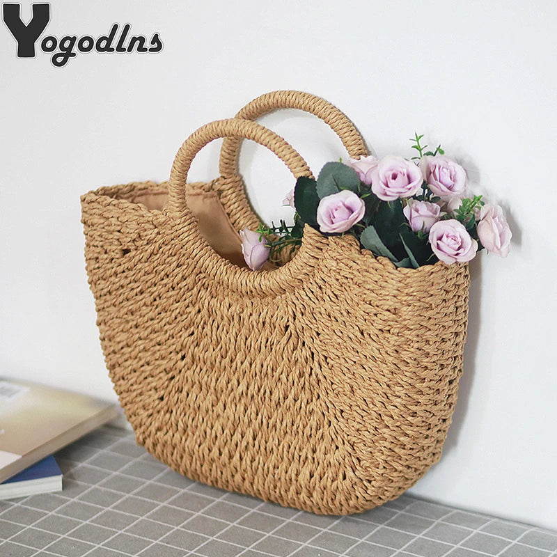 A handwoven straw moon bag with top handles in a natural tan color, displayed against a white background.