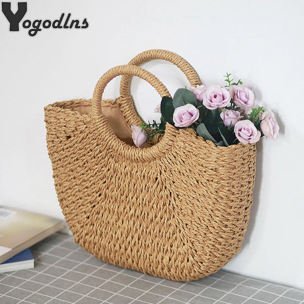 A handwoven straw moon bag with top handles in a natural tan color, displayed against a white background.
