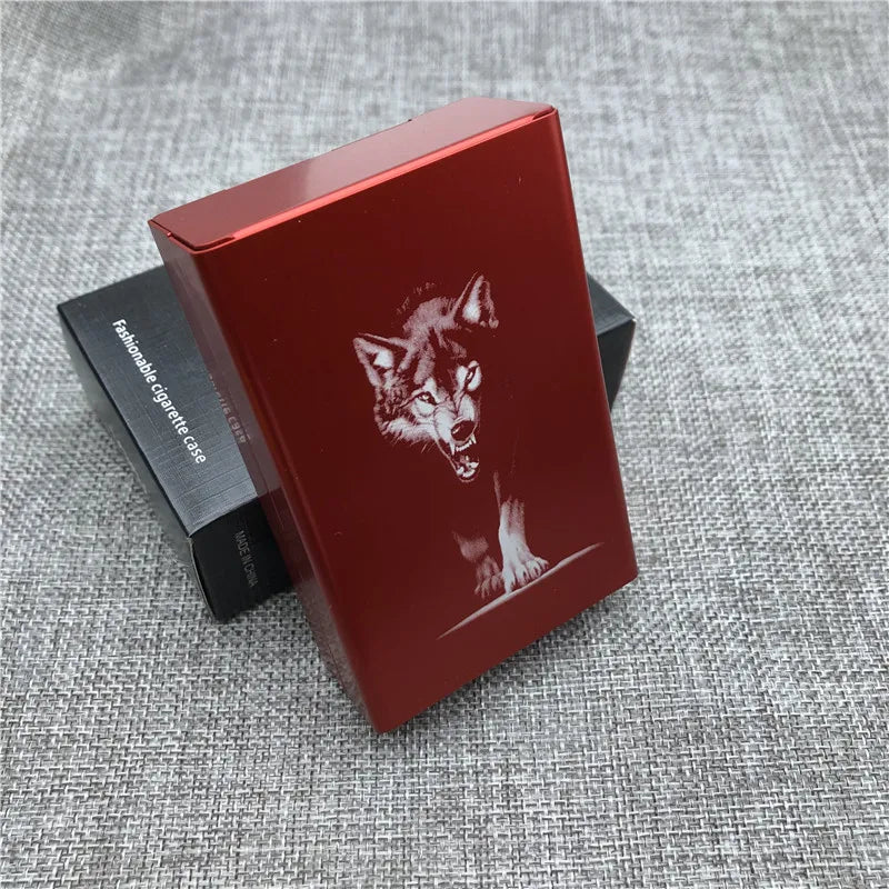 A red custom engraved cigarette case featuring a wolf head design, resting on a gray textured surface.