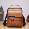 A brown vintage PU leather crossbody messenger bag with a leather handle and flap resting on a wooden surface.