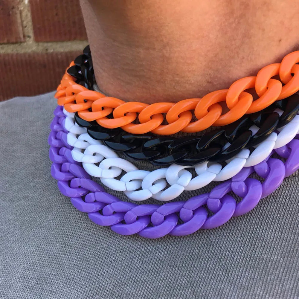 A close-up of a layered necklace featuring acrylic link chains in orange, black, white, and purple.