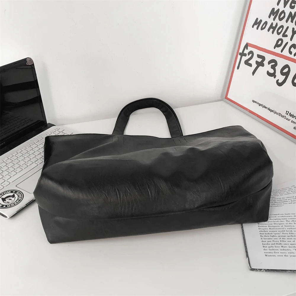 A black oversized PU leather tote bag with a handle is displayed on a white surface.