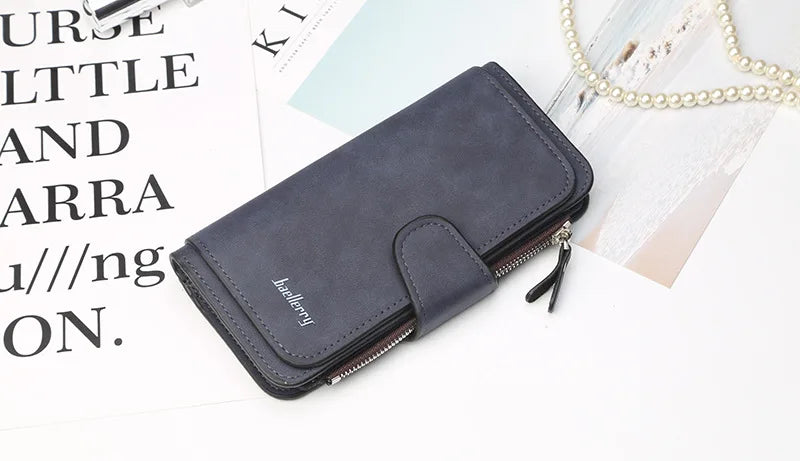 A dark blue leather card holder wallet lying on a white surface next to some papers and a pearl necklace.