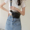 A woman models a black PU leather crossbody sling bag with a gold chain strap and a white top and denim skirt.