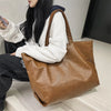 A woman holds an oversized brown PU leather tote bag with a zipper closure.