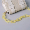 A beige woven shoulder bag with white straps and a yellow chain attached.