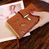 Cartera tipo clutch de cuero PU marrón con bordado de hoja de oro, sostenida en la mano sobre una superficie de madera.