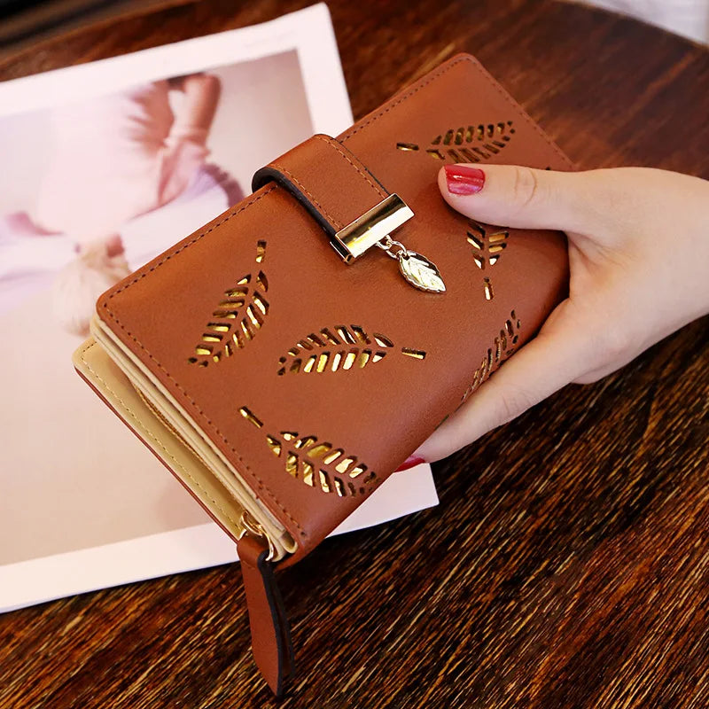 Cartera tipo clutch de cuero PU marrón con bordado de hoja de oro, sostenida en la mano sobre una superficie de madera.
