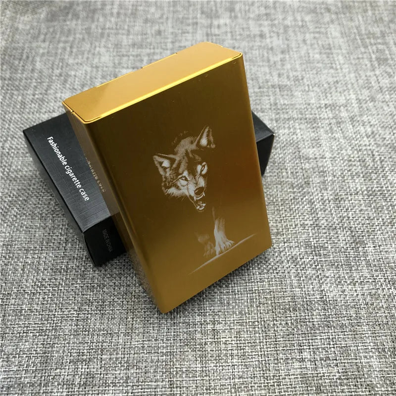 A gold cigarette case with a custom engraved wolf head design resting on a gray fabric surface.
