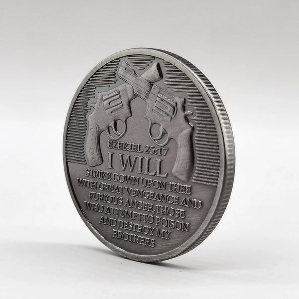 A silver-plated commemorative coin featuring a depiction of a gun and the text I WILL STRIKE DOWN UPON THEE WITH GREAT VENGEA