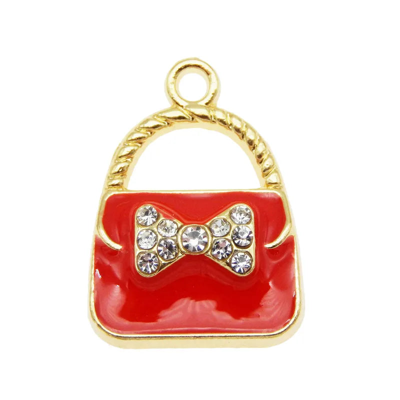 Pendentif charm doré en forme de sac à main avec corps émail rouge et nœud scintillant.