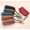 A collection of genuine cowhide leather double-zip wristlet wallets in various shades of black, blue, brown, and pink.