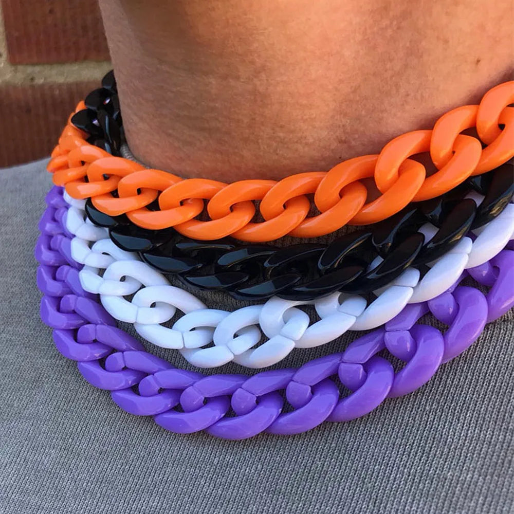 A stack of colorful acrylic link chain necklaces in orange, black, white, and purple displayed against a person's neck.